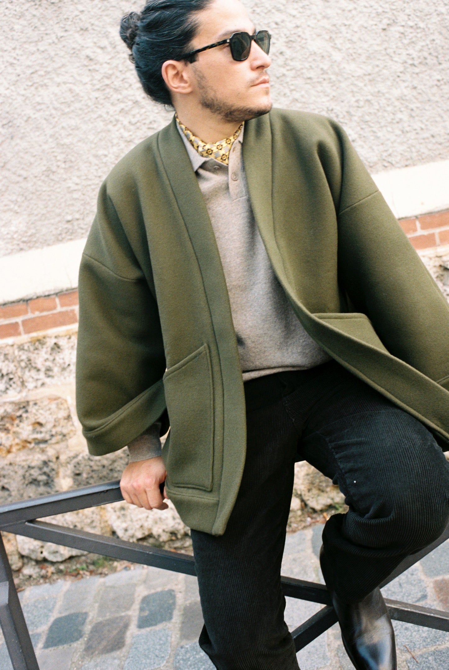 Homme portant le kimono RICHELIEU en laine et cachemire kaki d’Atelier Sarita, coupe veste avec grandes poches plaquées. Kimono structuré, fabriqué à la main à Paris dans un lainage italien issu de stocks dormants de maison de luxe. Modèle chaud, élégant et intemporel, photographié ans un style urbain parisien.