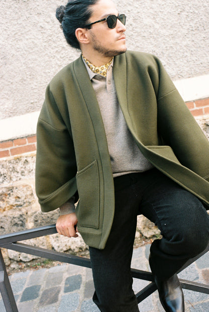 Homme portant le kimono RICHELIEU en laine et cachemire kaki d’Atelier Sarita, coupe veste avec grandes poches plaquées. Kimono structuré, fabriqué à la main à Paris dans un lainage italien issu de stocks dormants de maison de luxe. Modèle chaud, élégant et intemporel, photographié ans un style urbain parisien.