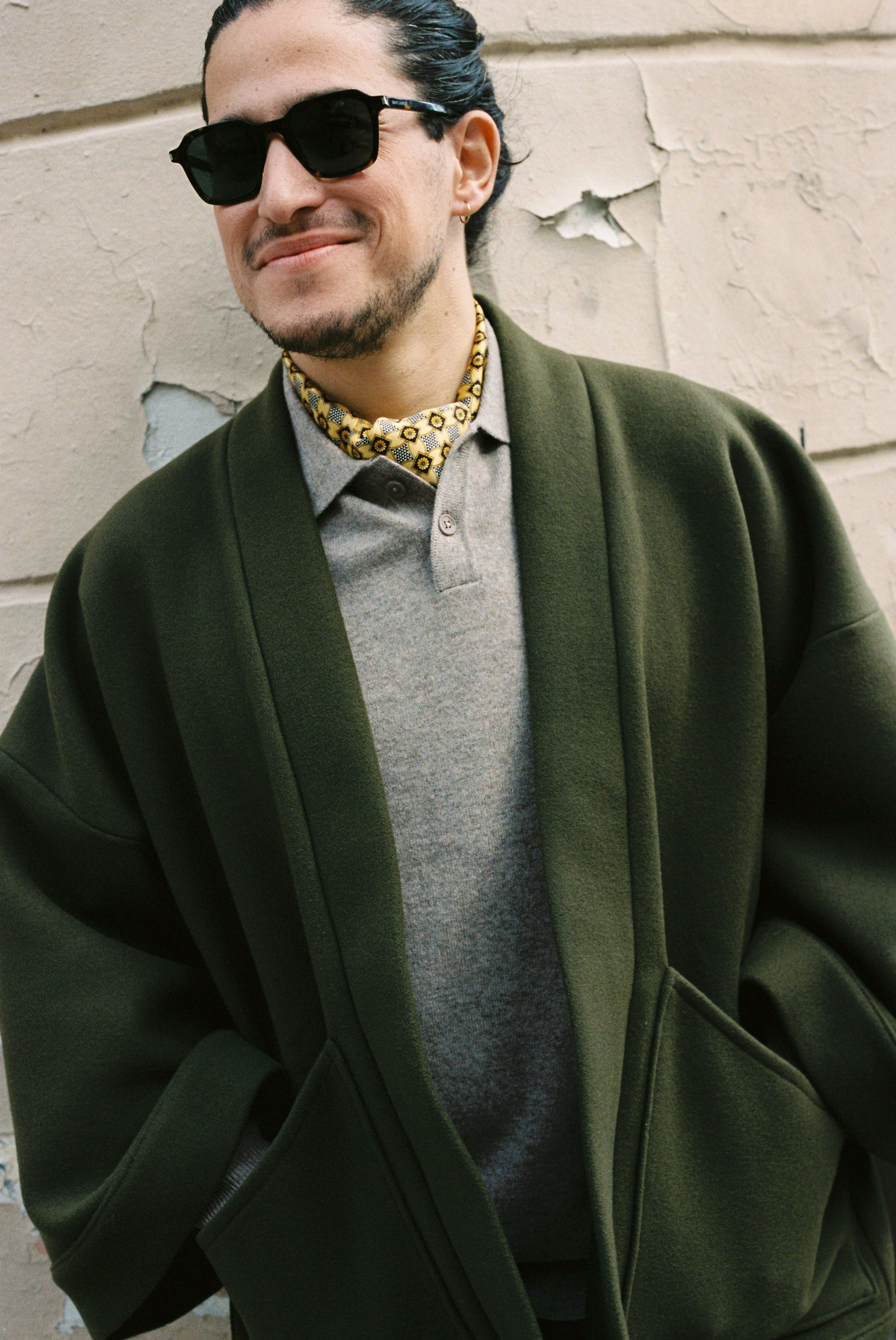 Homme portant le kimono RICHELIEU en laine et cachemire kaki d’Atelier Sarita, coupe veste avec grandes poches plaquées. Kimono structuré, fabriqué à la main à Paris dans un lainage italien issu de stocks dormants de maison de luxe. Modèle chaud, élégant et intemporel, photographié ans un style urbain parisien.