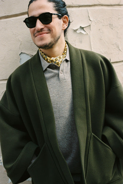 Homme portant le kimono RICHELIEU en laine et cachemire kaki d’Atelier Sarita, coupe veste avec grandes poches plaquées. Kimono structuré, fabriqué à la main à Paris dans un lainage italien issu de stocks dormants de maison de luxe. Modèle chaud, élégant et intemporel, photographié ans un style urbain parisien.