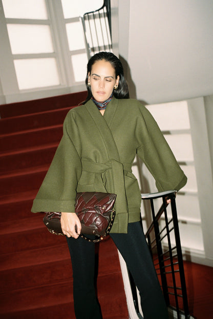 Femme portant le kimono RICHELIEU en laine et cachemire kaki d’Atelier Sarita, coupe veste avec grandes poches plaquées. Kimono structuré, fabriqué à la main à Paris dans un lainage italien issu de stocks dormants de maison de luxe. Modèle chaud, élégant et intemporel, photographié ans un style urbain parisien.