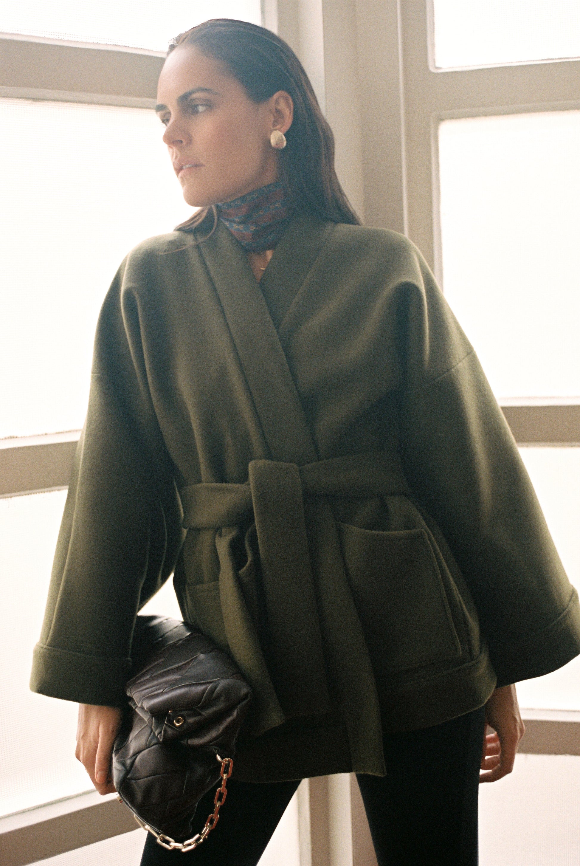 Femme portant le kimono RICHELIEU en laine et cachemire kaki d’Atelier Sarita, coupe veste avec grandes poches plaquées. Kimono structuré, fabriqué à la main à Paris dans un lainage italien issu de stocks dormants de maison de luxe. Modèle chaud, élégant et intemporel, photographié ans un style urbain parisien.