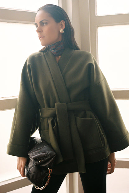 Femme portant le kimono RICHELIEU en laine et cachemire kaki d’Atelier Sarita, coupe veste avec grandes poches plaquées. Kimono structuré, fabriqué à la main à Paris dans un lainage italien issu de stocks dormants de maison de luxe. Modèle chaud, élégant et intemporel, photographié ans un style urbain parisien.