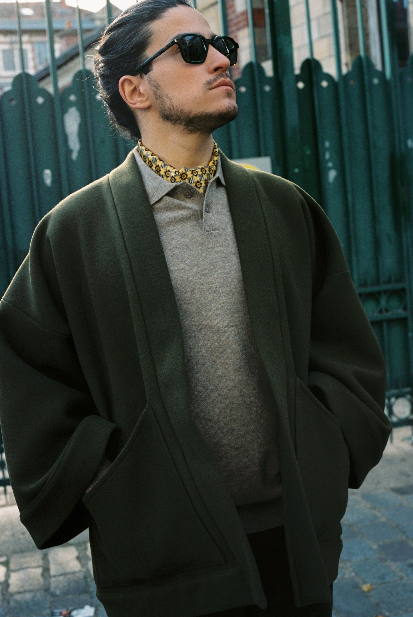 Homme portant le kimono RICHELIEU en laine et cachemire kaki d’Atelier Sarita, coupe veste avec grandes poches plaquées. Kimono structuré, fabriqué à la main à Paris dans un lainage italien issu de stocks dormants de maison de luxe. Modèle chaud, élégant et intemporel, photographié ans un style urbain parisien.