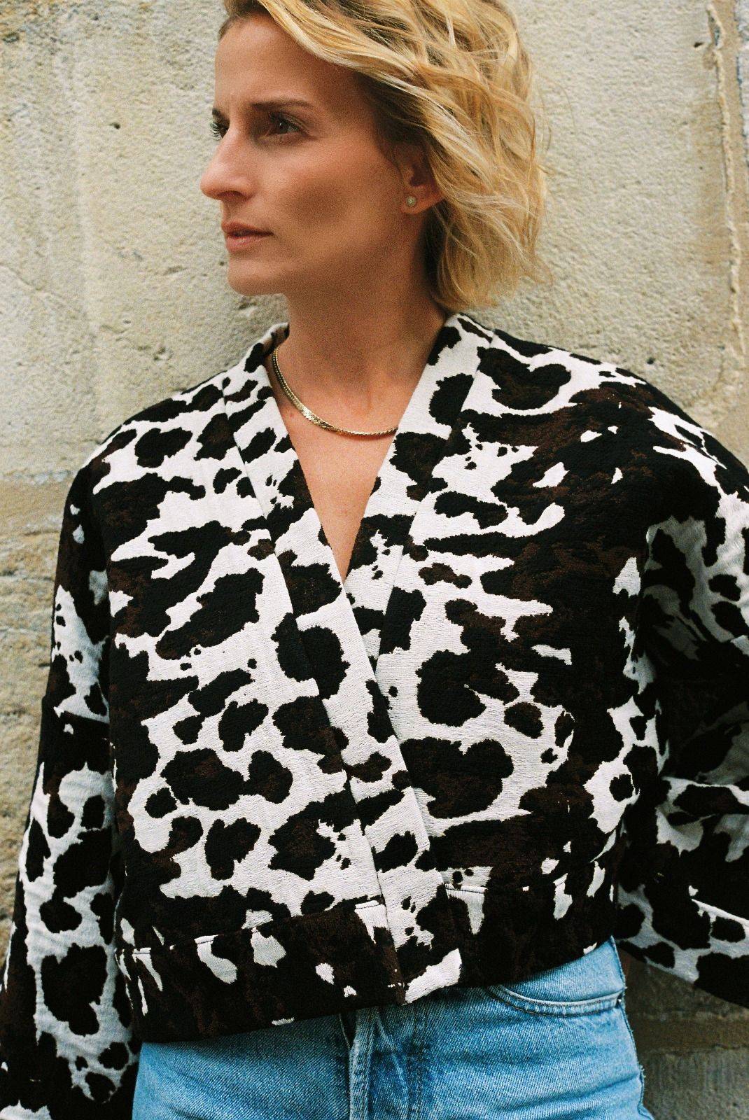Atelier Sarita – Kimono Roger en jacquard motif vache. Une coupe courte et audacieuse, pensée comme une pièce arty et urbaine, qui bouscule les codes du vestiaire parisien. Confectionné à la main à Paris en série limitée, ce kimono est réalisé dans un jacquard épais et texturé, issu d’une maison textile française reconnue pour son savoir-faire et son exigence en matière de durabilité. Une pièce singulière qui célèbre l’originalité et le mouvement urbain.