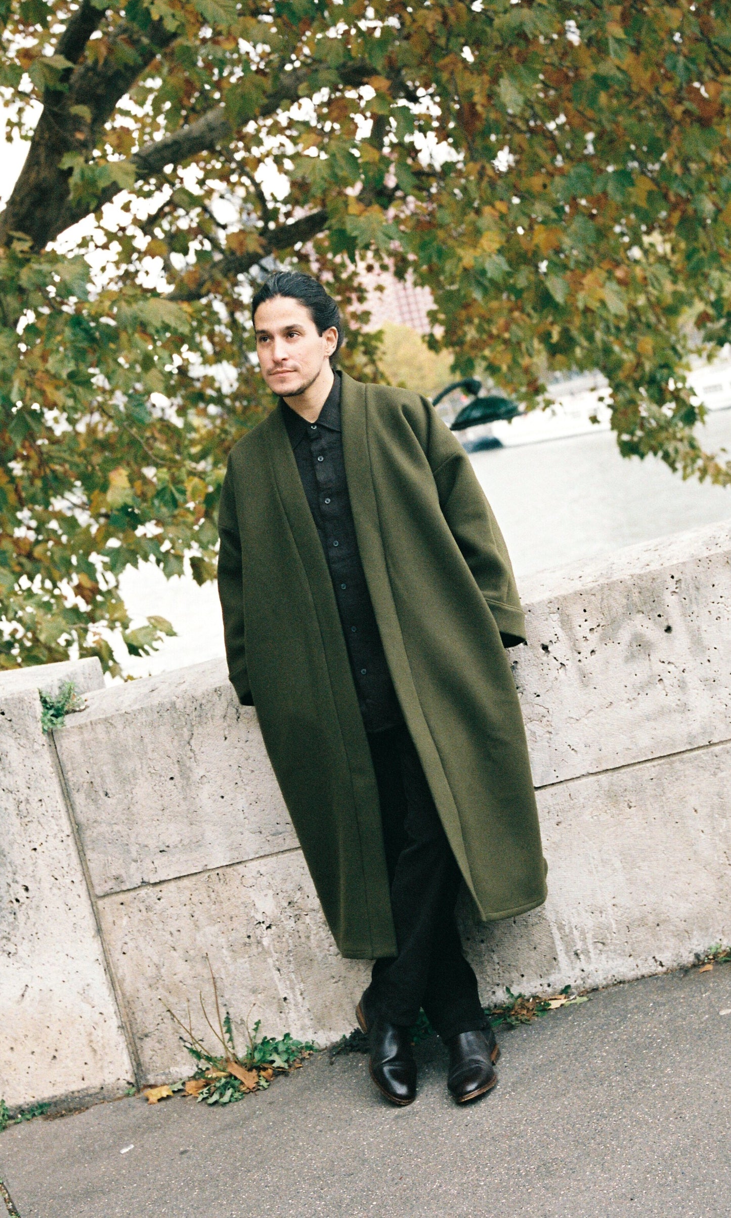 Homme portant le kimono long VIVIENNE en laine et cachemire kaki d’Atelier Sarita. Kimono oversize et structuré, fabriqué à la main à Paris dans un lainage italien issu de stocks dormants de maison de luxe. Pièce enveloppante et élégante, photographiée en extérieur avec la tour Eiffel en arrière-plan, mettant en valeur la douceur, la tenue et la chaleur du tissu.