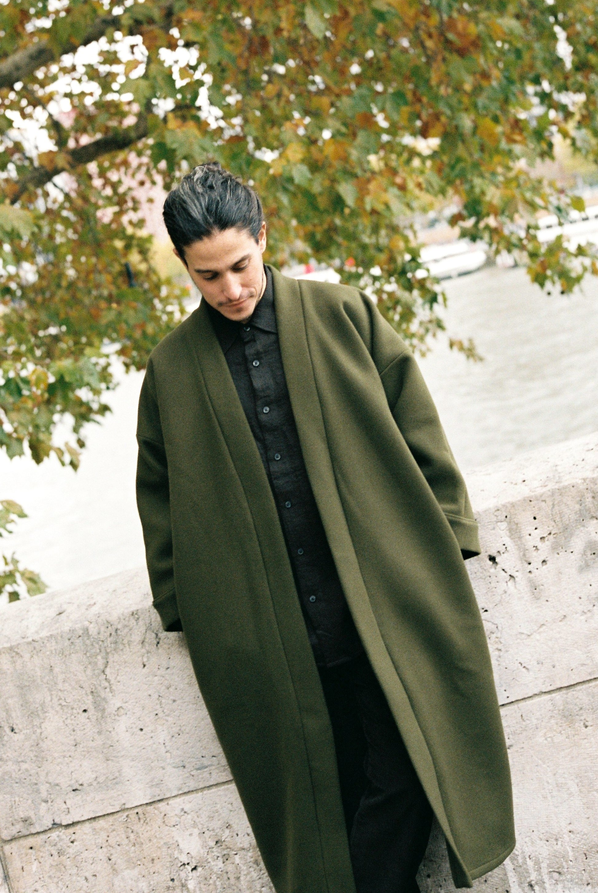 Homme portant le kimono long VIVIENNE en laine et cachemire kaki d’Atelier Sarita. Kimono oversize et structuré, fabriqué à la main à Paris dans un lainage italien issu de stocks dormants de maison de luxe. Pièce enveloppante et élégante, photographiée en extérieur avec la tour Eiffel en arrière-plan, mettant en valeur la douceur, la tenue et la chaleur du tissu.