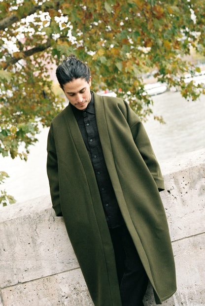 Homme portant le kimono long VIVIENNE en laine et cachemire kaki d’Atelier Sarita. Kimono oversize et structuré, fabriqué à la main à Paris dans un lainage italien issu de stocks dormants de maison de luxe. Pièce enveloppante et élégante, photographiée en extérieur avec la tour Eiffel en arrière-plan, mettant en valeur la douceur, la tenue et la chaleur du tissu.