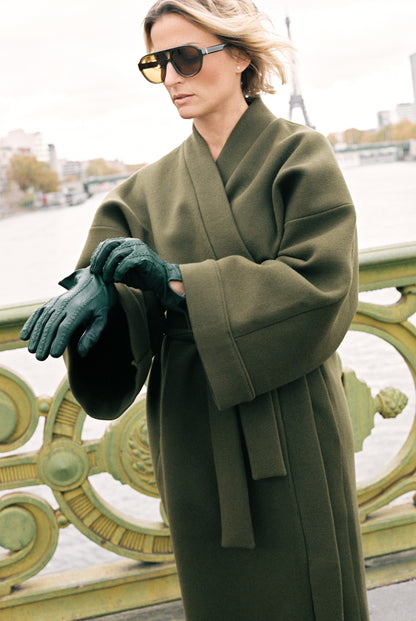 Femme portant le kimono long VIVIENNE en laine et cachemire kaki d’Atelier Sarita. Kimono oversize et structuré, fabriqué à la main à Paris dans un lainage italien issu de stocks dormants de maison de luxe. Pièce enveloppante et élégante, photographiée en extérieur avec la tour Eiffel en arrière-plan, mettant en valeur la douceur, la tenue et la chaleur du tissu.