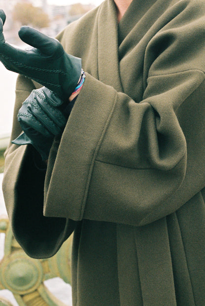Femme portant le kimono long VIVIENNE en laine et cachemire kaki d’Atelier Sarita. Kimono oversize et structuré, fabriqué à la main à Paris dans un lainage italien issu de stocks dormants de maison de luxe. Pièce enveloppante et élégante, photographiée en extérieur avec la tour Eiffel en arrière-plan, mettant en valeur la douceur, la tenue et la chaleur du tissu.