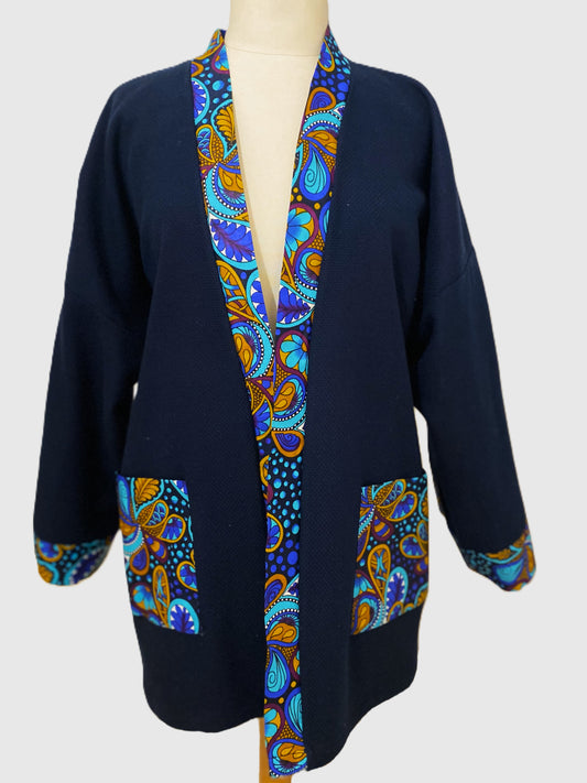 Kimono court en coton bleu avec finitions en wax coloré, manches larges et poches assorties, présenté sur un mannequin.