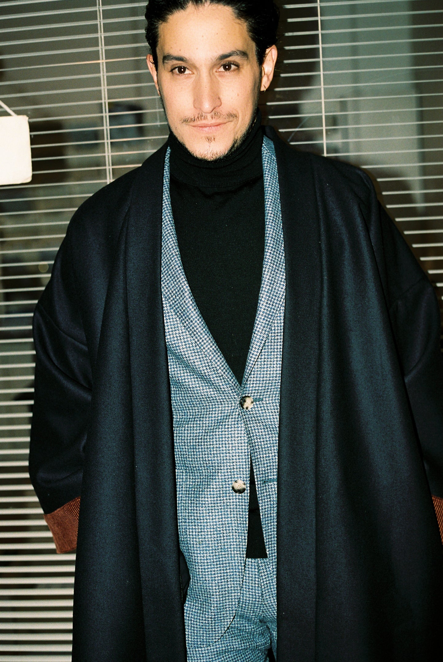 Homme portant le kimono long COLBERT Atelier Sarita en laine caviar noire avec finitions en velours coton couleur oud. Modèle ample et architectural, confectionné à la main à Paris, pensé comme un manteau kimono hivernal unisexe.