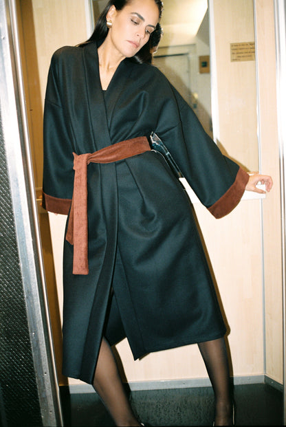 Femme portant le kimono long COLBERT Atelier Sarita en laine caviar noire avec finitions en velours coton couleur oud. Modèle ample et architectural, confectionné à la main à Paris, pensé comme un manteau kimono hivernal unisexe.
