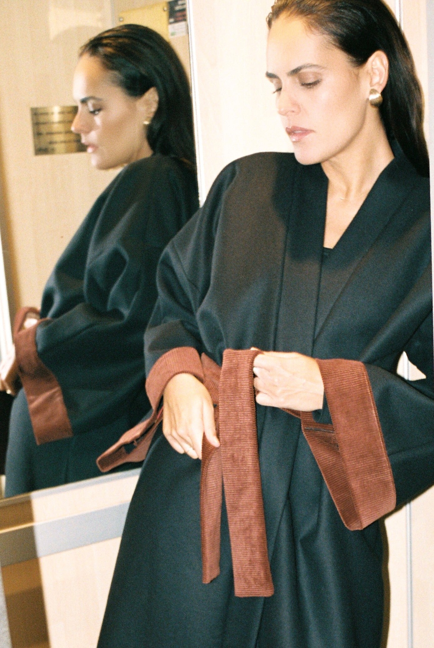 Femme portant le kimono long COLBERT Atelier Sarita en laine caviar noire avec finitions en velours coton couleur oud. Modèle ample et architectural, confectionné à la main à Paris, pensé comme un manteau kimono hivernal unisexe.