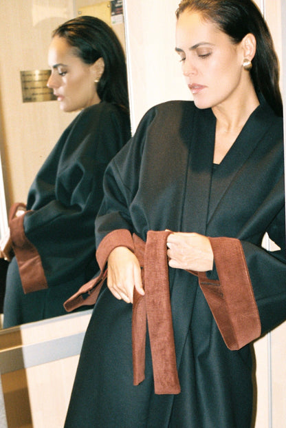 Femme portant le kimono long COLBERT Atelier Sarita en laine caviar noire avec finitions en velours coton couleur oud. Modèle ample et architectural, confectionné à la main à Paris, pensé comme un manteau kimono hivernal unisexe.