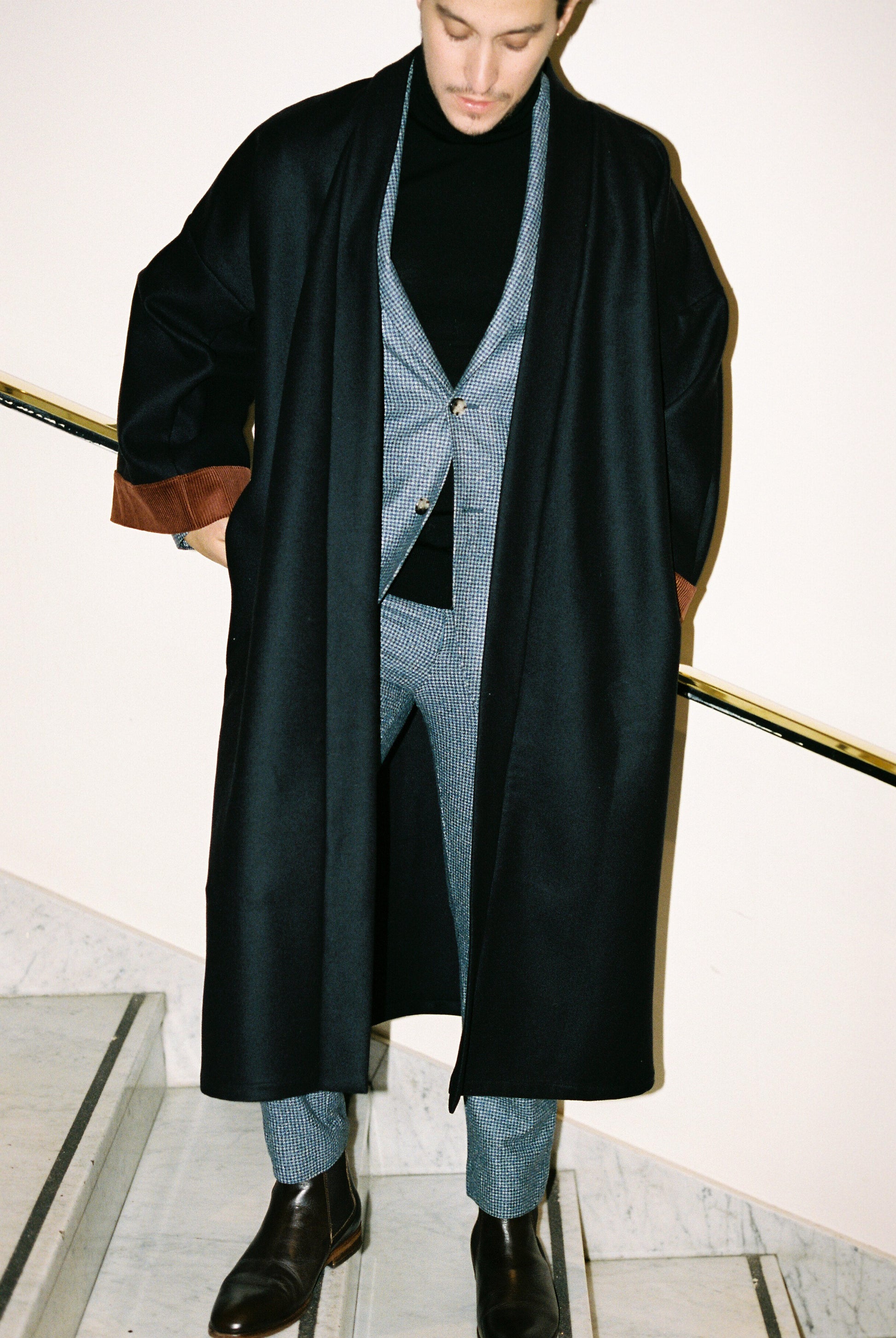 Homme portant le kimono long COLBERT Atelier Sarita en laine caviar noire avec finitions en velours coton couleur oud. Modèle ample et architectural, confectionné à la main à Paris, pensé comme un manteau kimono hivernal unisexe.