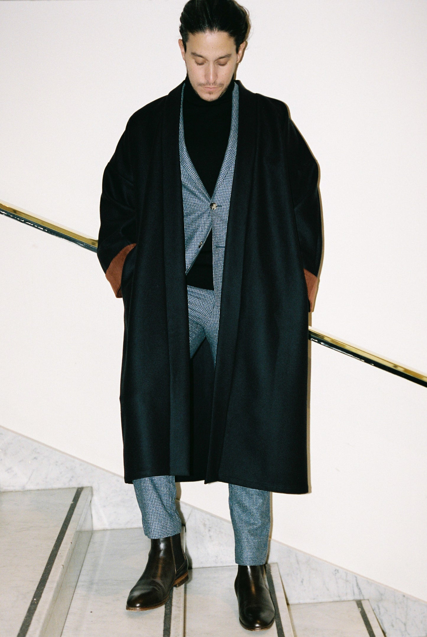 Homme portant le kimono long COLBERT Atelier Sarita en laine caviar noire avec finitions en velours coton couleur oud. Modèle ample et architectural, confectionné à la main à Paris, pensé comme un manteau kimono hivernal unisexe.