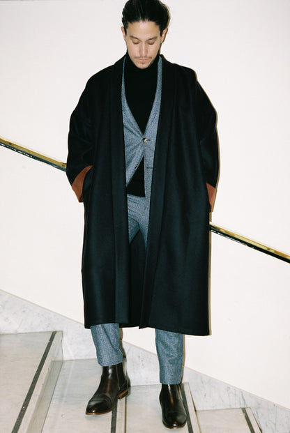 Homme portant le kimono long COLBERT Atelier Sarita en laine caviar noire avec finitions en velours coton couleur oud. Modèle ample et architectural, confectionné à la main à Paris, pensé comme un manteau kimono hivernal unisexe.