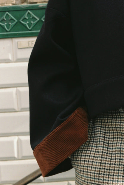 Femme portant le kimono VÉRO Atelier Sarita, un kimono court en laine noire caviar avec finitions en velours coton couleur oud, photographié dans une entrée de métro parisien. Modèle au style architectural et urbain, confectionné à la main à Paris.