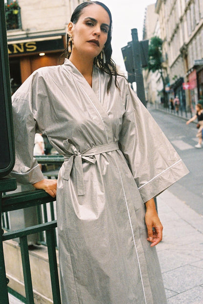 Atelier Sarita – Kimono Crystal en popeline de coton argenté. Long kimono fluide à la coupe affirmée, ceinturé à la taille, confectionné à la main à Paris en série limitée. Une pièce audacieuse et urbaine, inspirée des reflets minéraux et des lumières de l’architecture parisienne.