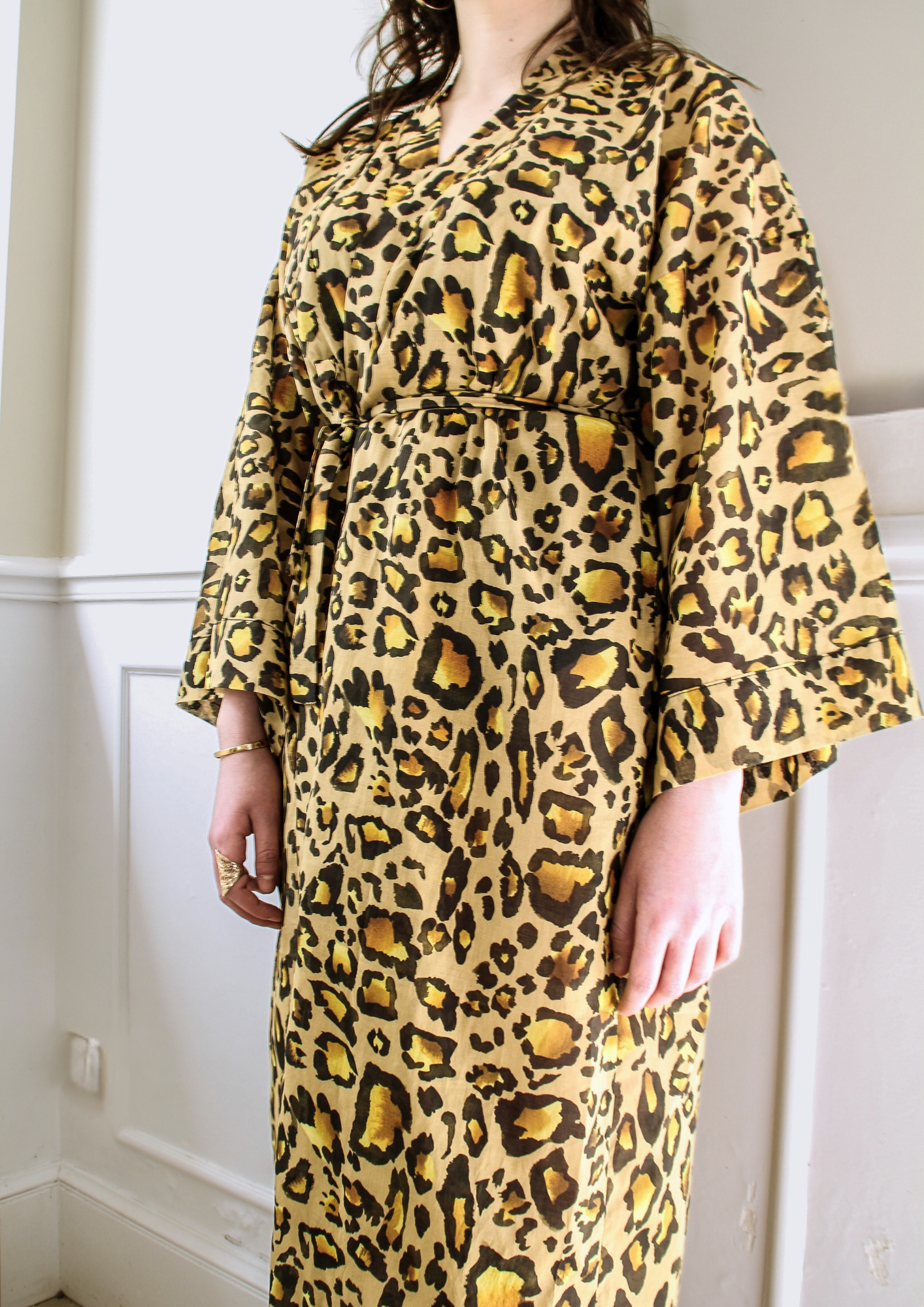 Femme portant un kimono long en voile de coton motif léopard, noué à la taille, dans une pièce lumineuse.