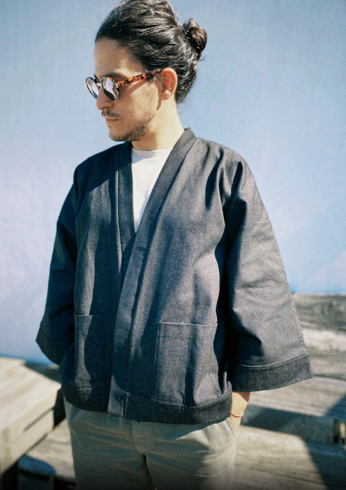 Homme portant un kimono court en denim noir 100% coton, avec manches larges et poches plaquées, fait à la main à Paris. 