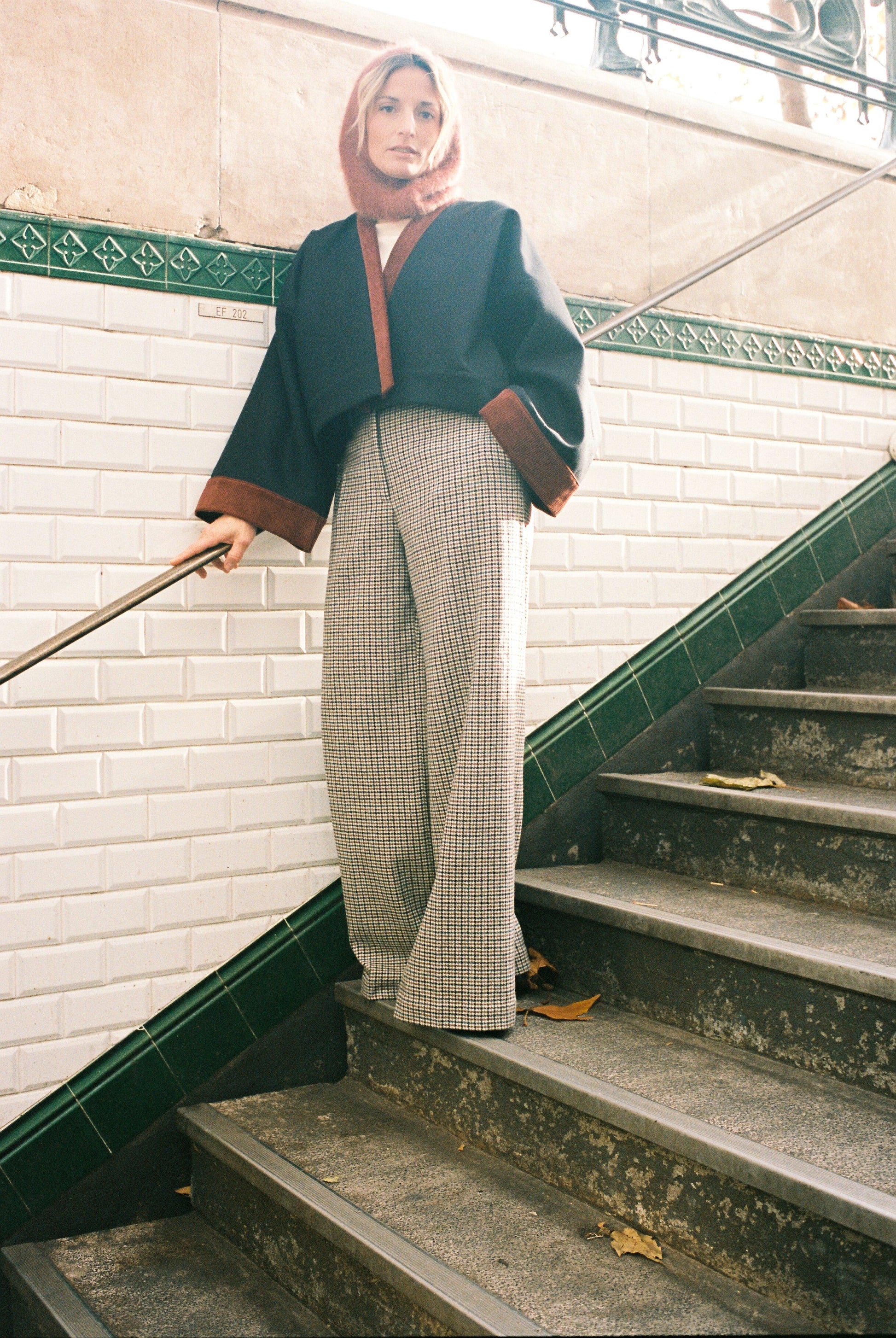 Femme portant le kimono VÉRO Atelier Sarita, un kimono court en laine noire caviar avec finitions en velours coton couleur oud, photographié dans une entrée de métro parisien. Modèle au style architectural et urbain, confectionné à la main à Paris.