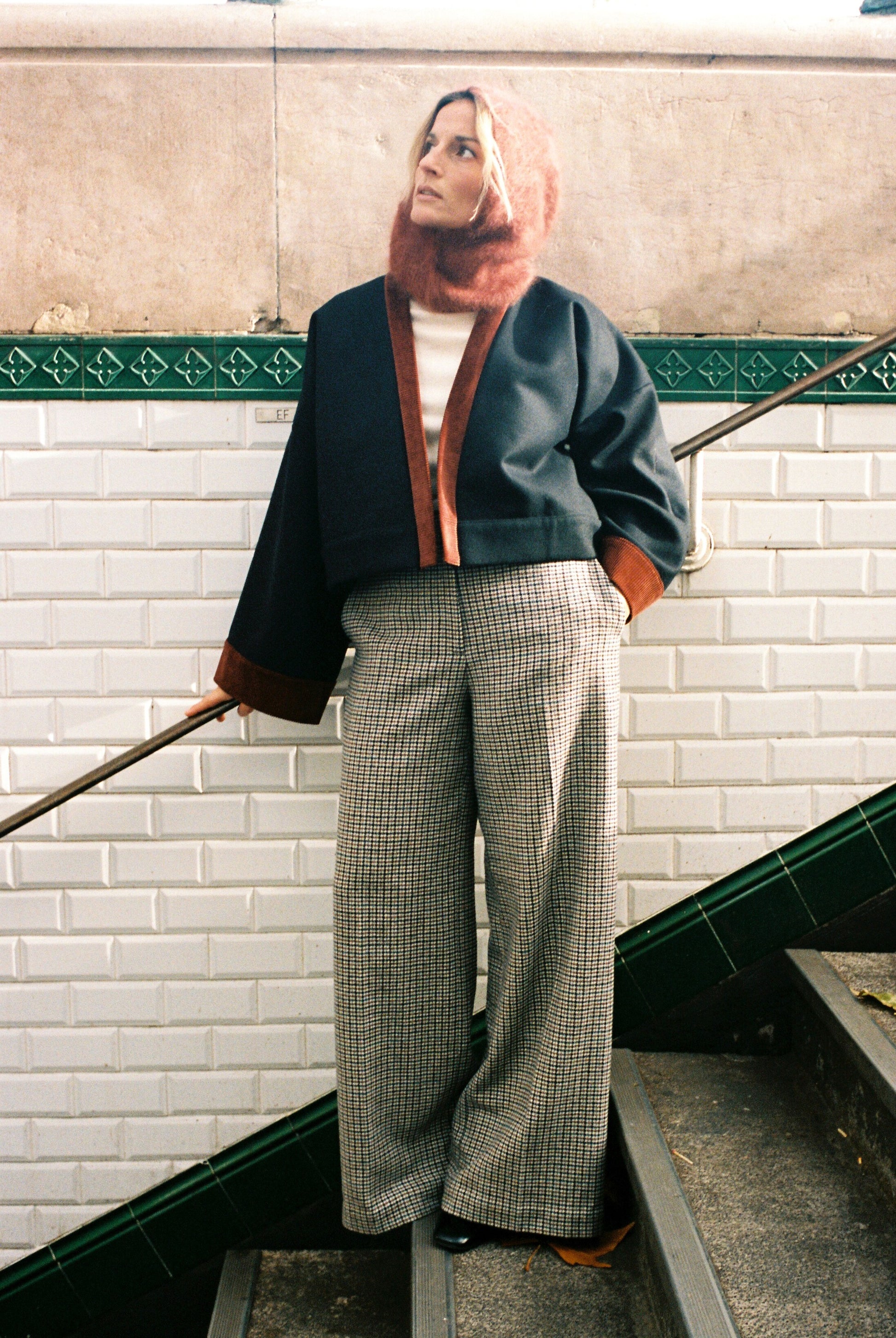 Femme portant le kimono VÉRO Atelier Sarita, un kimono court en laine noire caviar avec finitions en velours coton couleur oud, photographié dans une entrée de métro parisien. Modèle au style architectural et urbain, confectionné à la main à Paris.
