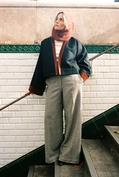 Femme portant le kimono VÉRO Atelier Sarita, un kimono court en laine noire caviar avec finitions en velours coton couleur oud, photographié dans une entrée de métro parisien. Modèle au style architectural et urbain, confectionné à la main à Paris.
