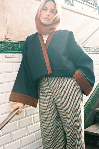 Femme portant le kimono VÉRO Atelier Sarita, un kimono court en laine noire caviar avec finitions en velours coton couleur oud, photographié dans une entrée de métro parisien. Modèle au style architectural et urbain, confectionné à la main à Paris.