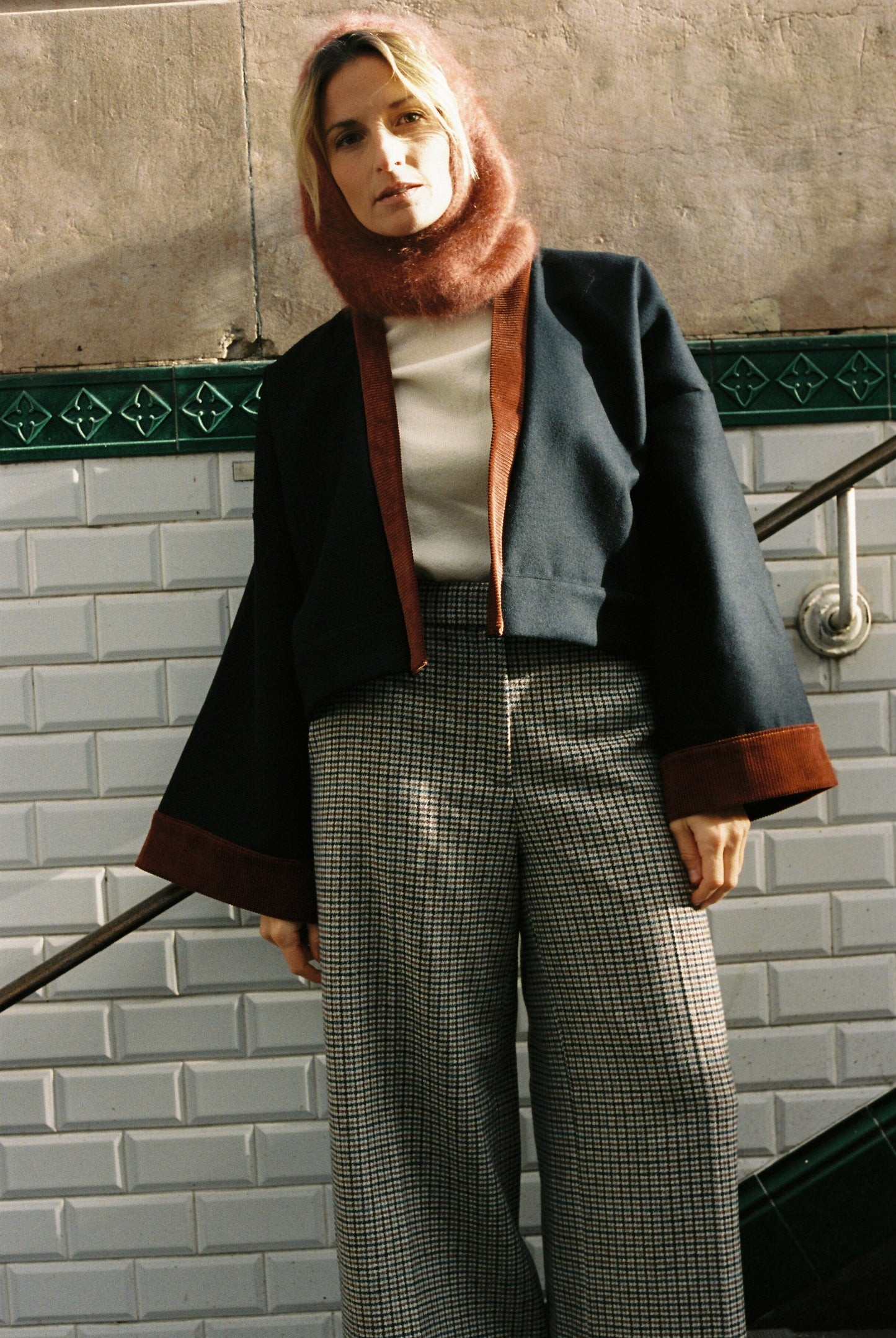 Femme portant le kimono VÉRO Atelier Sarita, un kimono court en laine noire caviar avec finitions en velours coton couleur oud, photographié dans une entrée de métro parisien. Modèle au style architectural et urbain, confectionné à la main à Paris.