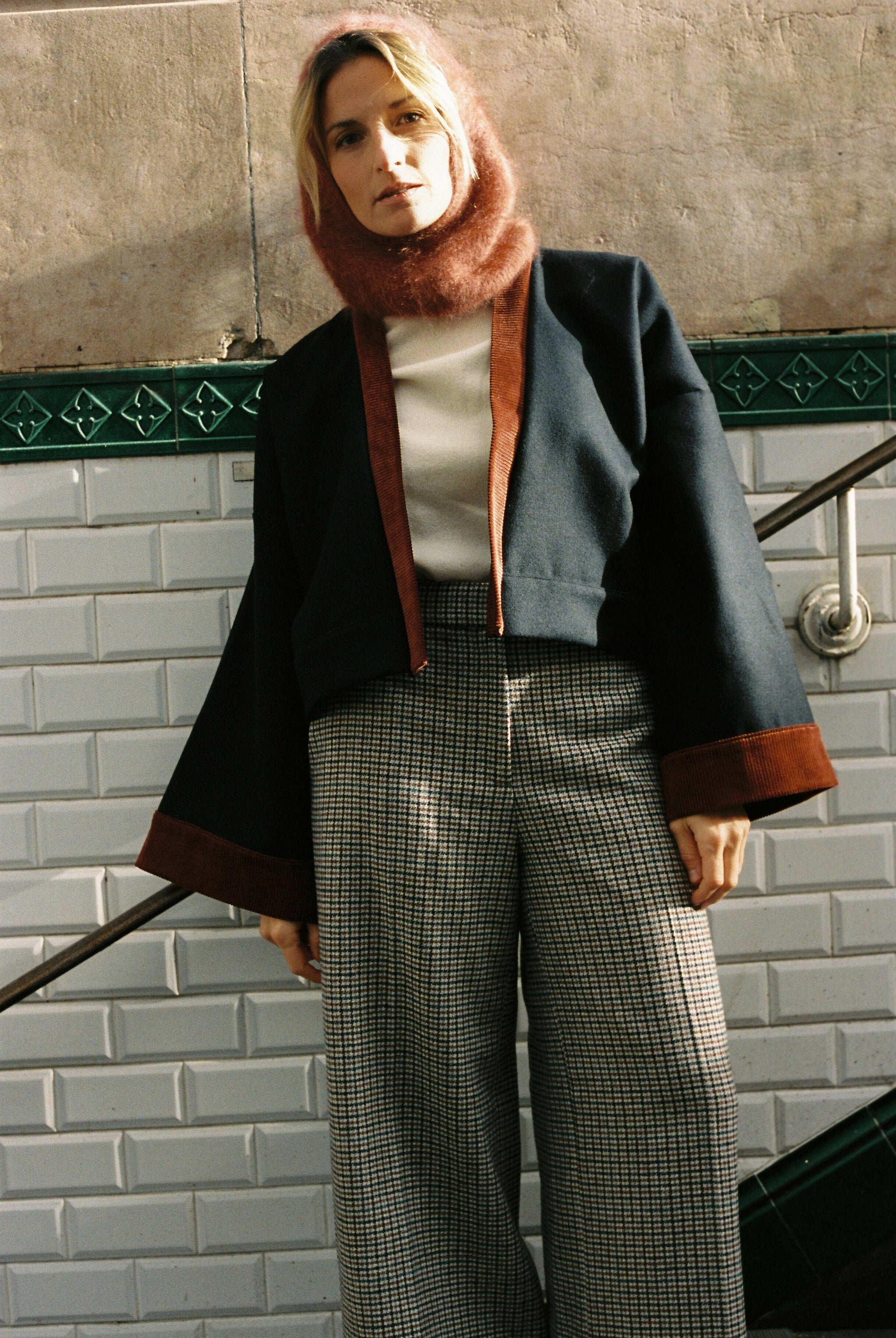 Femme portant le kimono VÉRO Atelier Sarita, un kimono court en laine noire caviar avec finitions en velours coton couleur oud, photographié dans une entrée de métro parisien. Modèle au style architectural et urbain, confectionné à la main à Paris.