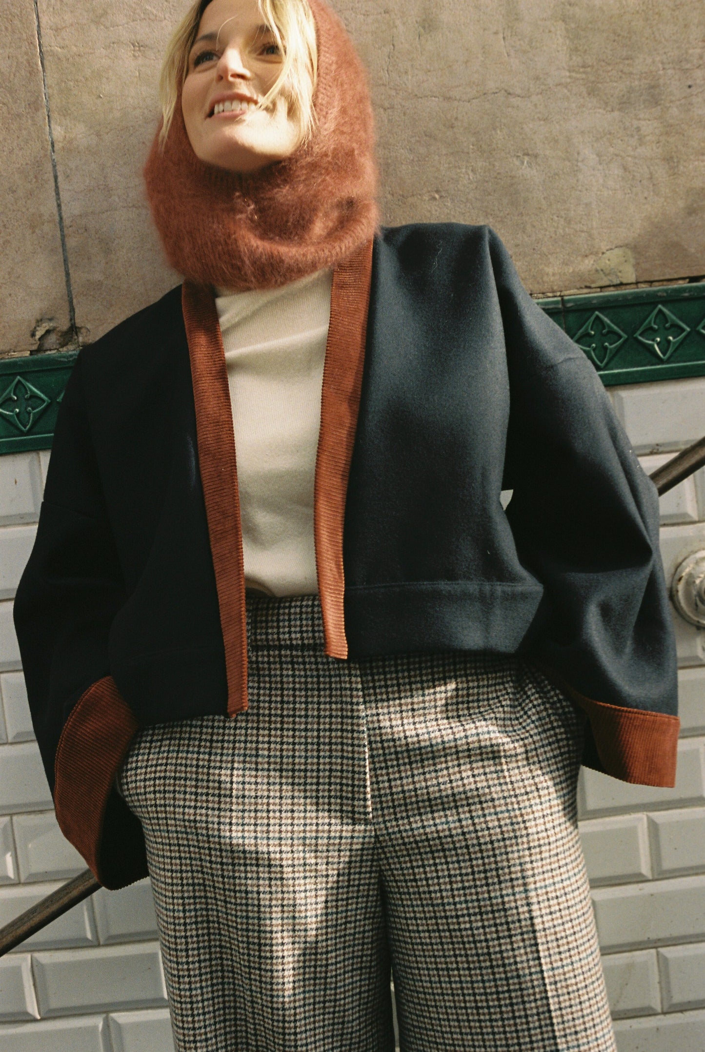 Femme portant le kimono VÉRO Atelier Sarita, un kimono court en laine noire caviar avec finitions en velours coton couleur oud, photographié dans une entrée de métro parisien. Modèle au style architectural et urbain, confectionné à la main à Paris.
