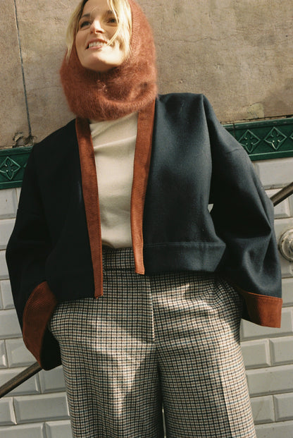 Femme portant le kimono VÉRO Atelier Sarita, un kimono court en laine noire caviar avec finitions en velours coton couleur oud, photographié dans une entrée de métro parisien. Modèle au style architectural et urbain, confectionné à la main à Paris.