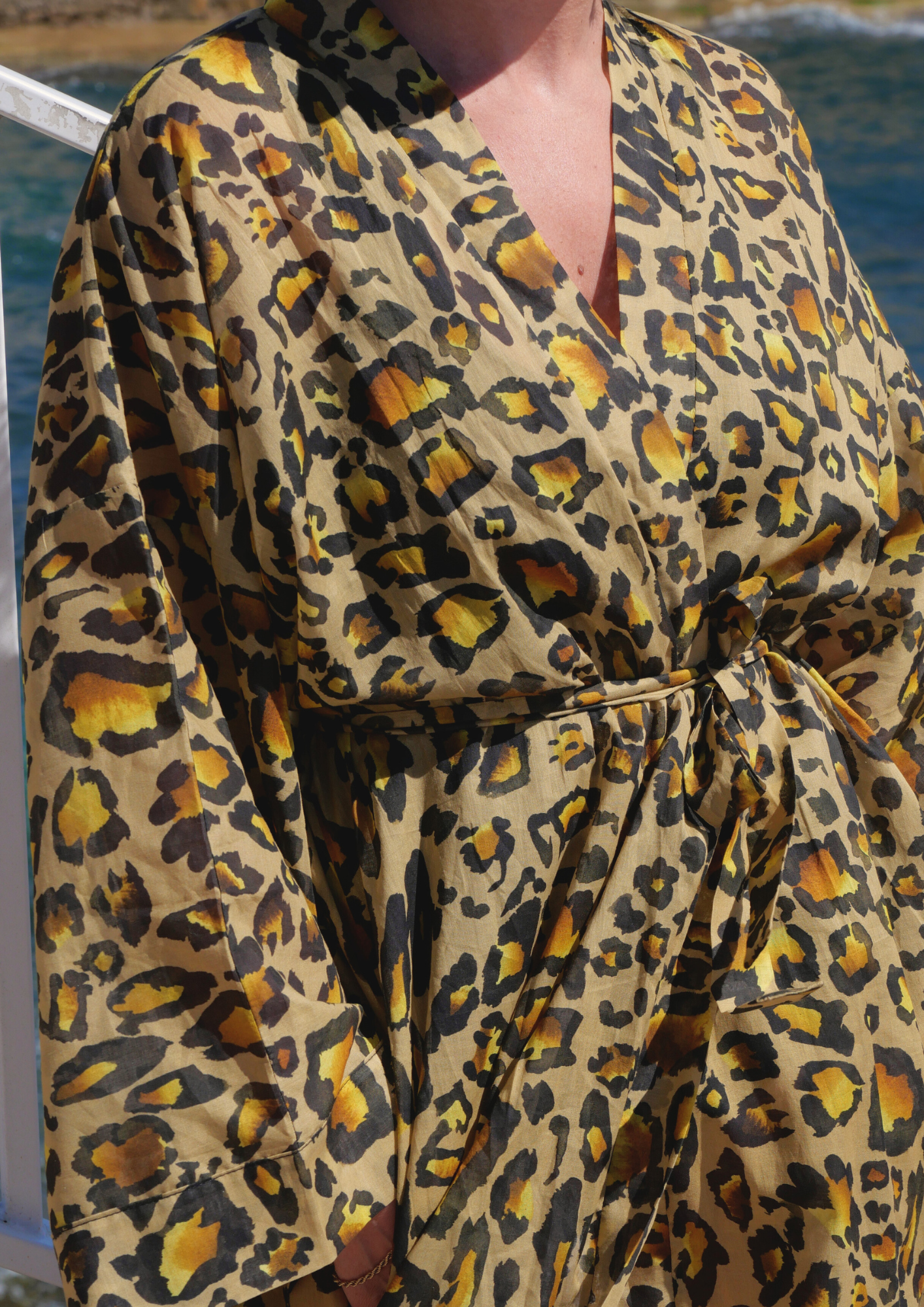 Femme portant un kimono long en voile de coton à imprimé léopard, ceinturé à la taille, posant face à la mer sous le soleil – création Atelier Sarita, confectionnée à la main à Paris.