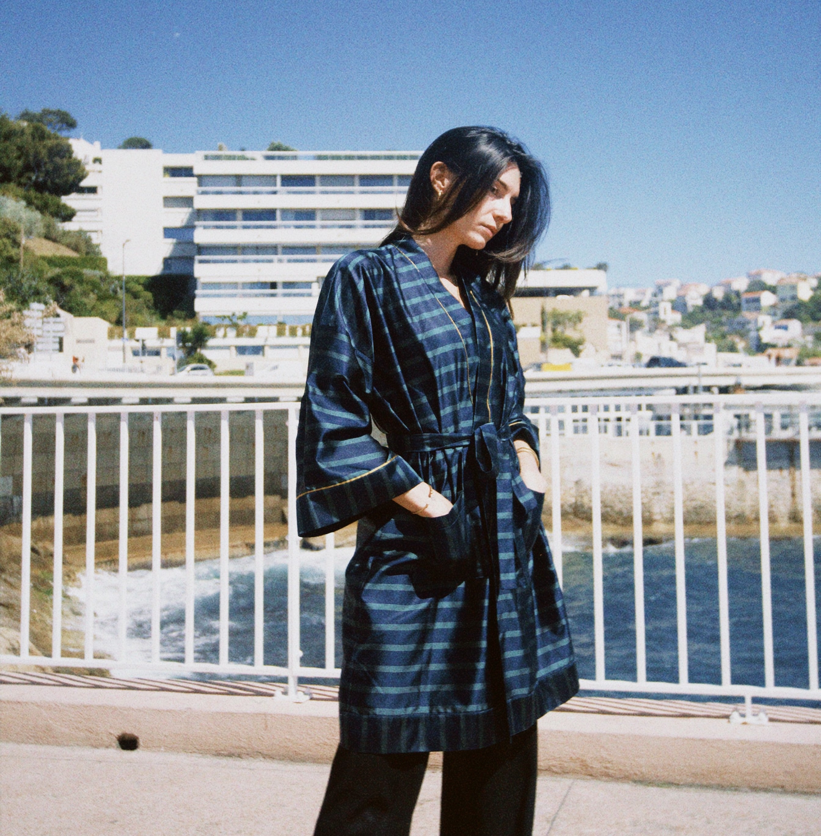 jeune femme dans un décor urbain mais balnéaire qui porte un kimono en soie bleu et vert. Une pièce unique faite à la main à Paris