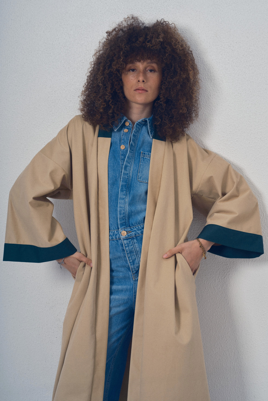 Trench beige aux lignes kimono avec finitions vert foncé porté ceinturé, modèle Charlot de la collection Côté Marais par Atelier Sarita.