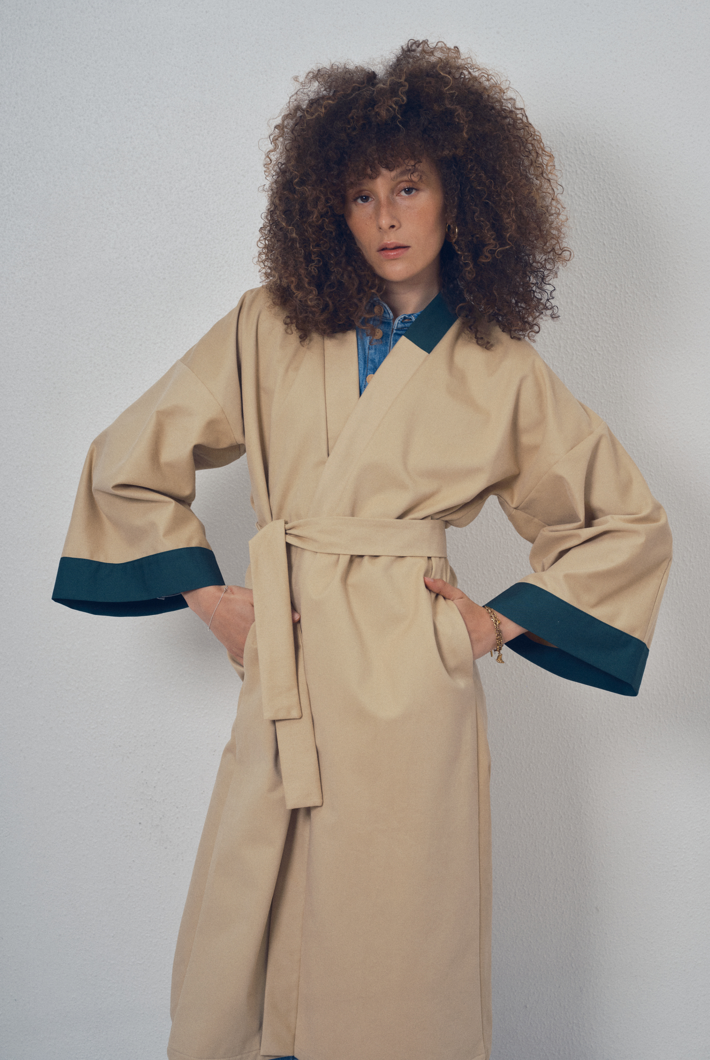 Trench beige aux lignes kimono avec finitions vert foncé porté ceinturé, modèle Charlot de la collection Côté Marais par Atelier Sarita.