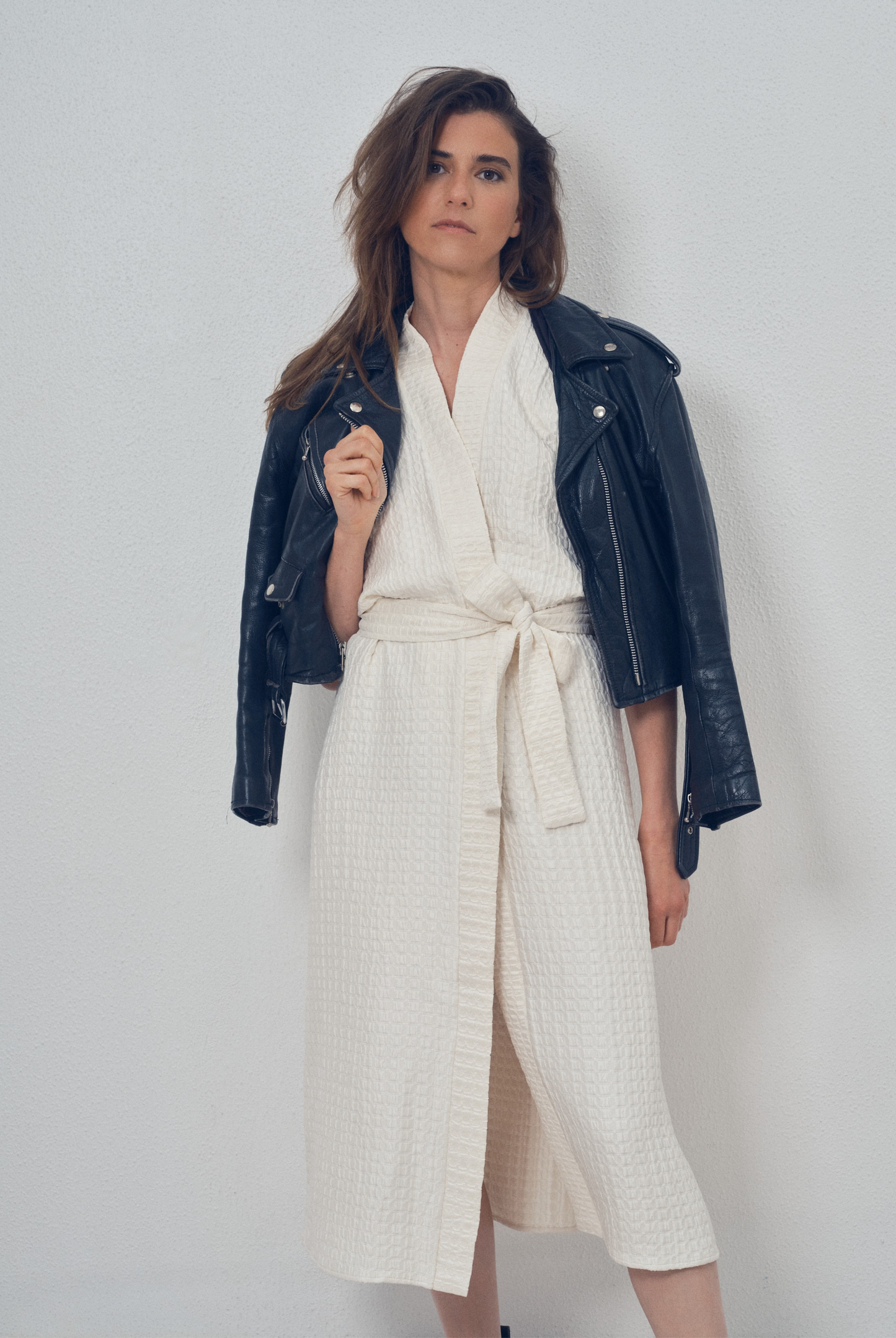 Robe portefeuille blanche en soie texturée portée avec des bottines noires et un perfecto en cuir noir, modèle Pastourelle de la collection Côté Marais par Atelier Sarita.