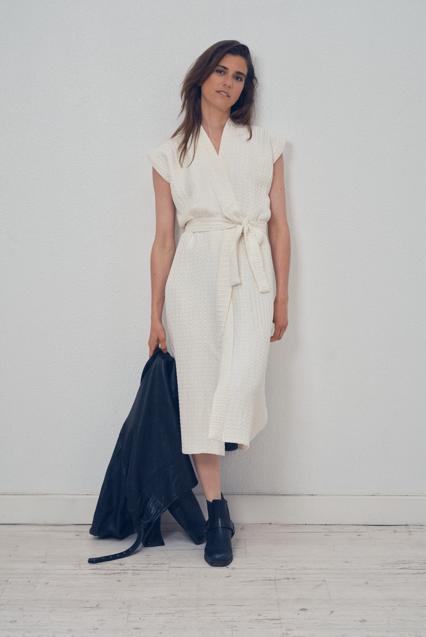 Robe portefeuille blanche en soie texturée portée avec des bottines noires et un perfecto en cuir noir, modèle Pastourelle de la collection Côté Marais par Atelier Sarita.