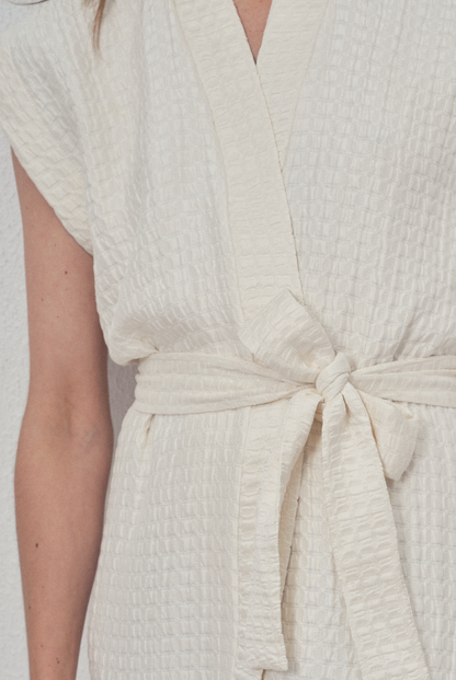 Robe portefeuille blanche en soie texturée portée avec des bottines noires et un perfecto en cuir noir, modèle Pastourelle de la collection Côté Marais par Atelier Sarita.