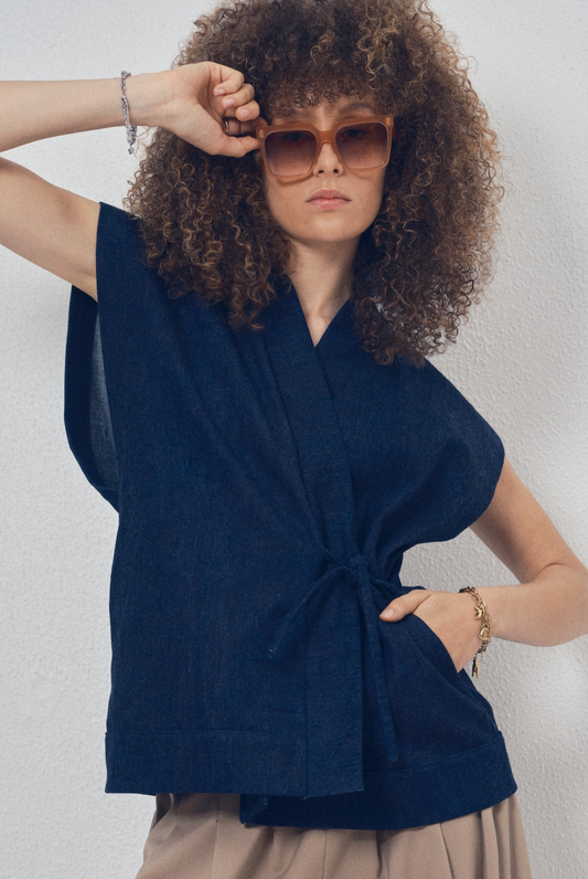 Pièce sans manches en denim bleu aux lignes kimono portée avec un pantalon ample beige, modèle Perla de la collection Côté Marais par Atelier Sarita.