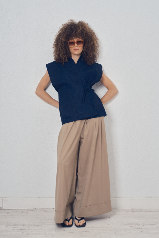 Pièce sans manches en denim bleu aux lignes kimono portée avec un pantalon ample beige, modèle Perla de la collection Côté Marais par Atelier Sarita.