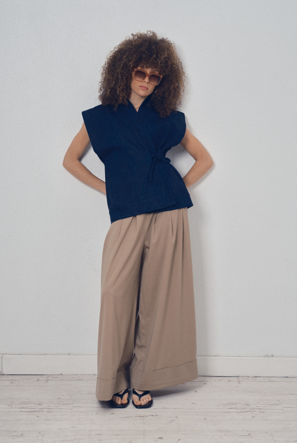 Pièce sans manches en denim bleu aux lignes kimono portée avec un pantalon ample beige, modèle Perla de la collection Côté Marais par Atelier Sarita.