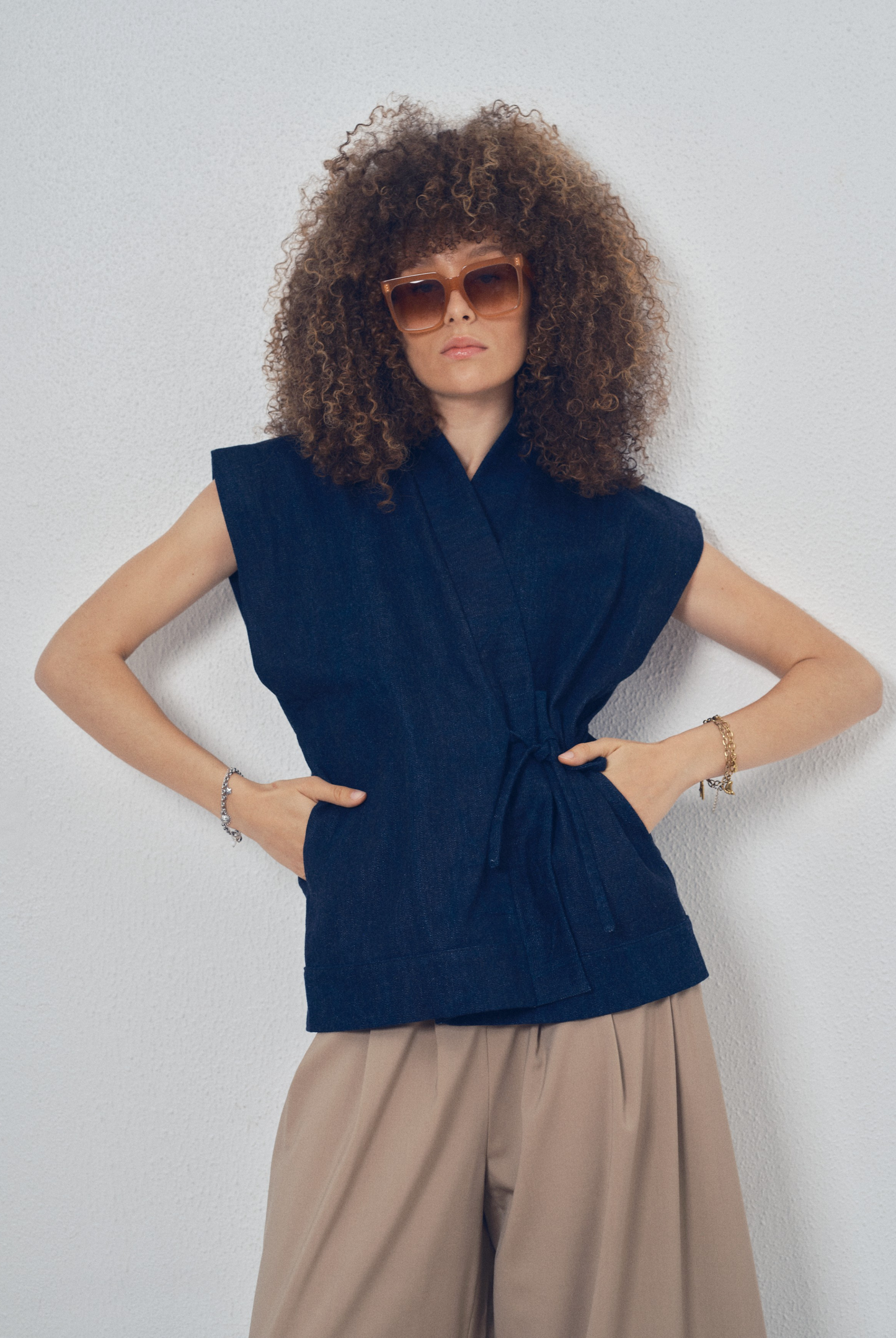 Pièce sans manches en denim bleu aux lignes kimono portée avec un pantalon ample beige, modèle Perla de la collection Côté Marais par Atelier Sarita.