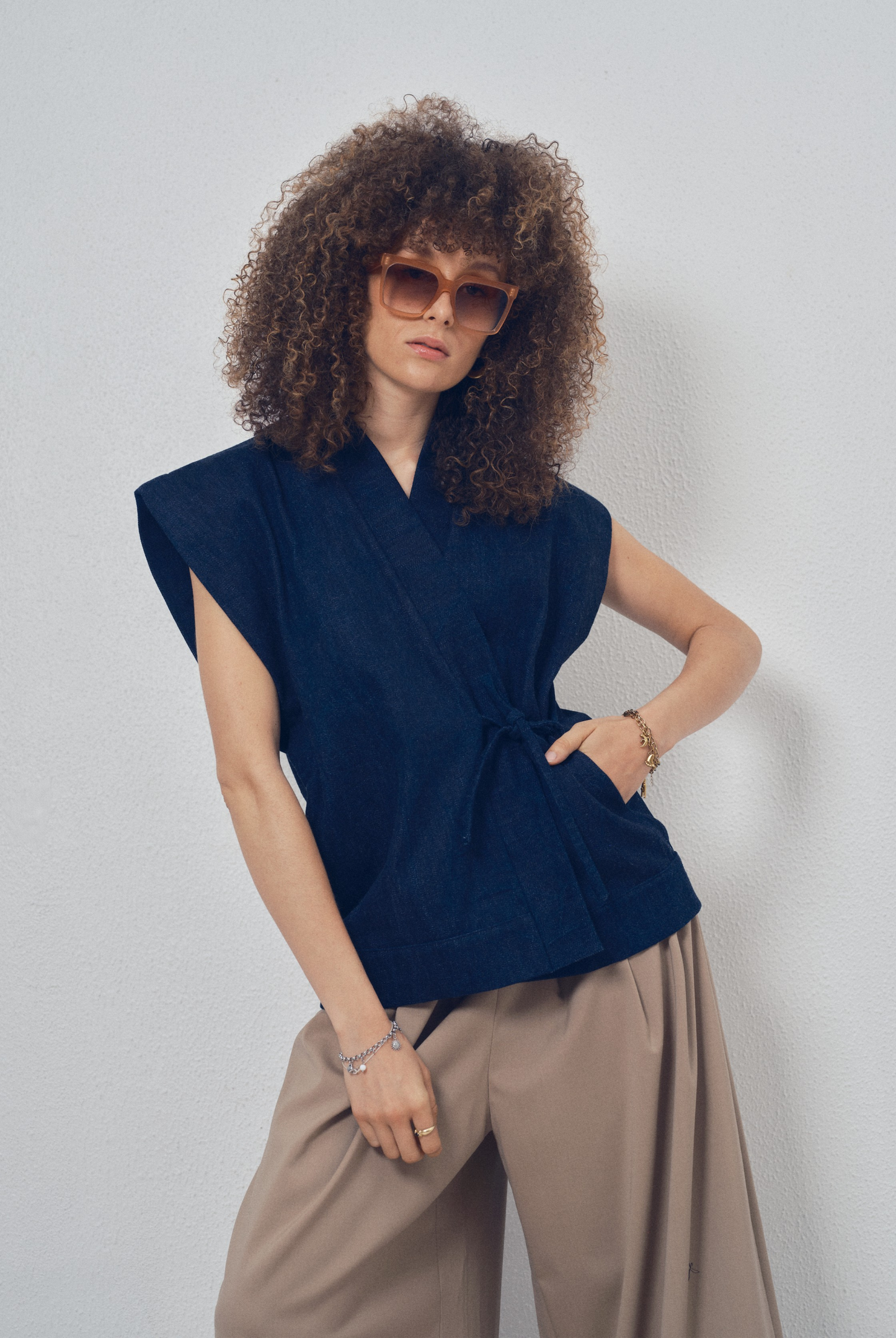 Pièce sans manches en denim bleu aux lignes kimono portée avec un pantalon ample beige, modèle Perla de la collection Côté Marais par Atelier Sarita.