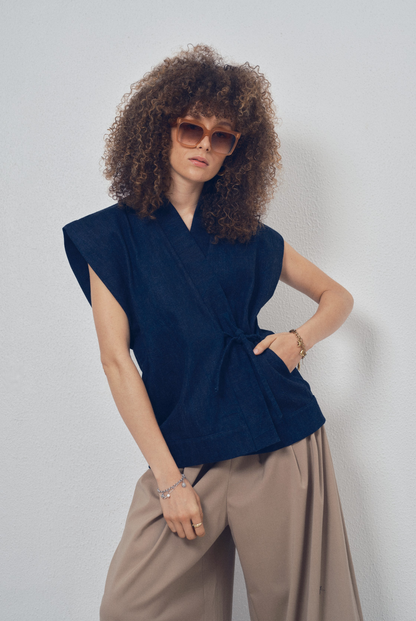 Pièce sans manches en denim bleu aux lignes kimono portée avec un pantalon ample beige, modèle Perla de la collection Côté Marais par Atelier Sarita.