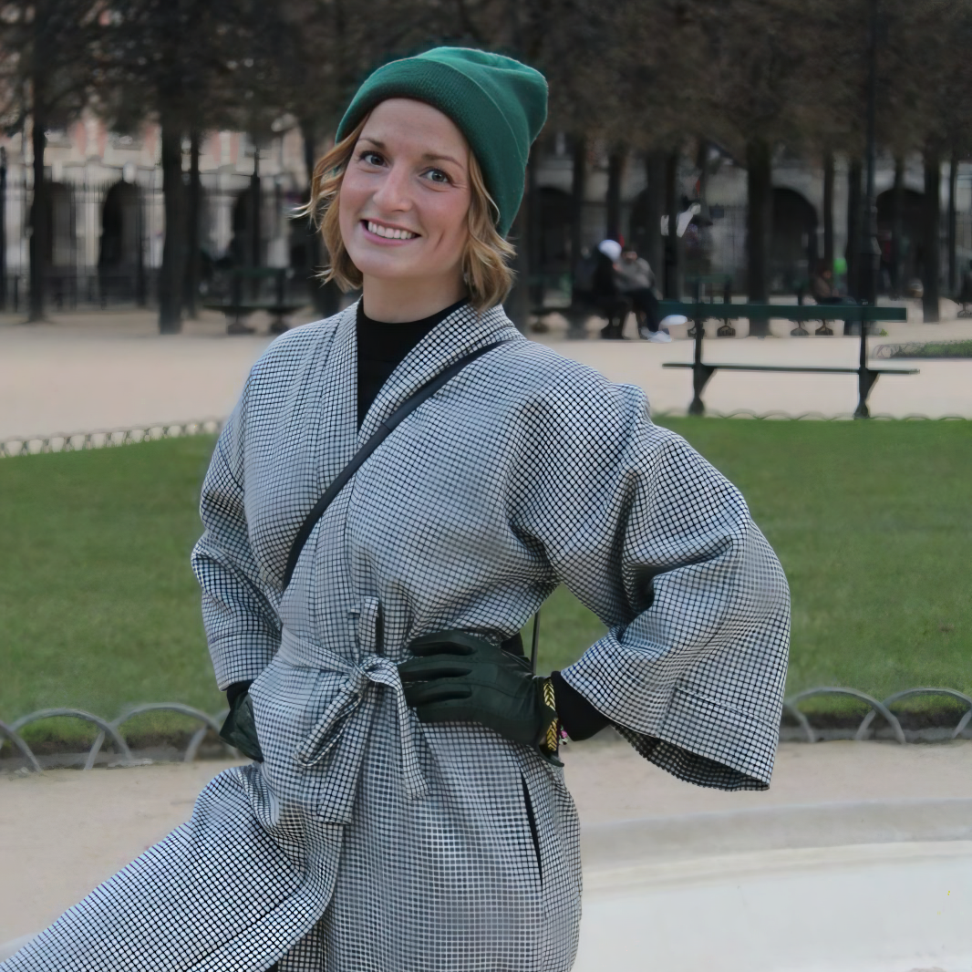 Sarah, fondatrice d'Atelier Sarita, souriante et rayonnante dans un kimono en vichy noir et blanc. Une image capturant l’élégance intemporelle et l’authenticité de la mode artisanale, dans un cadre parisien emblématique, la Place des Vosges. 